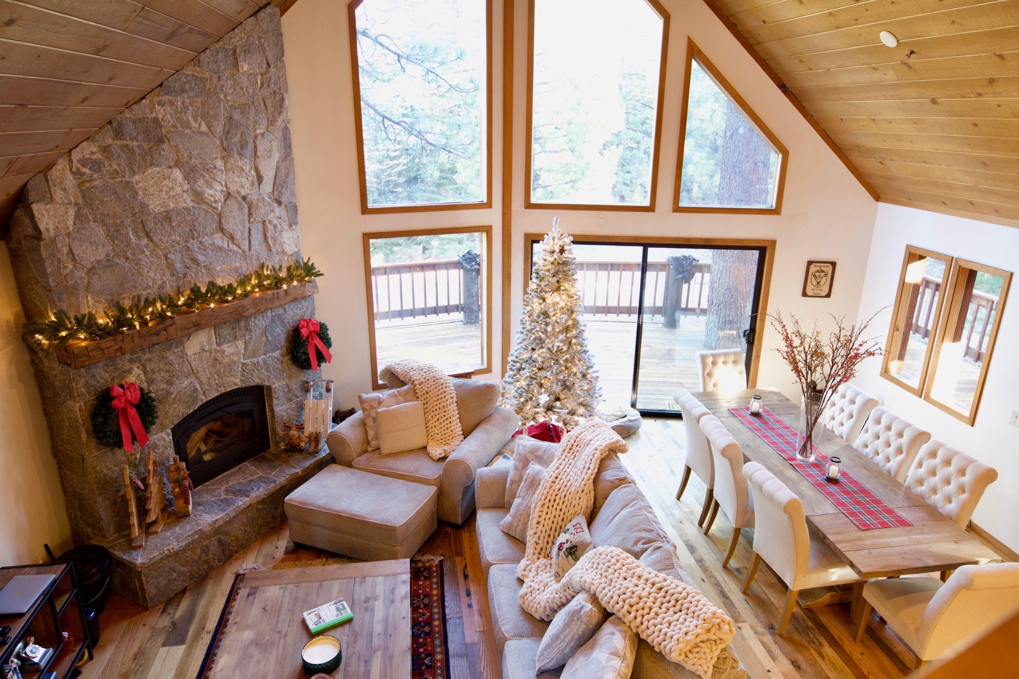 Large open great room with welcoming fireplace, dining table and tall windows